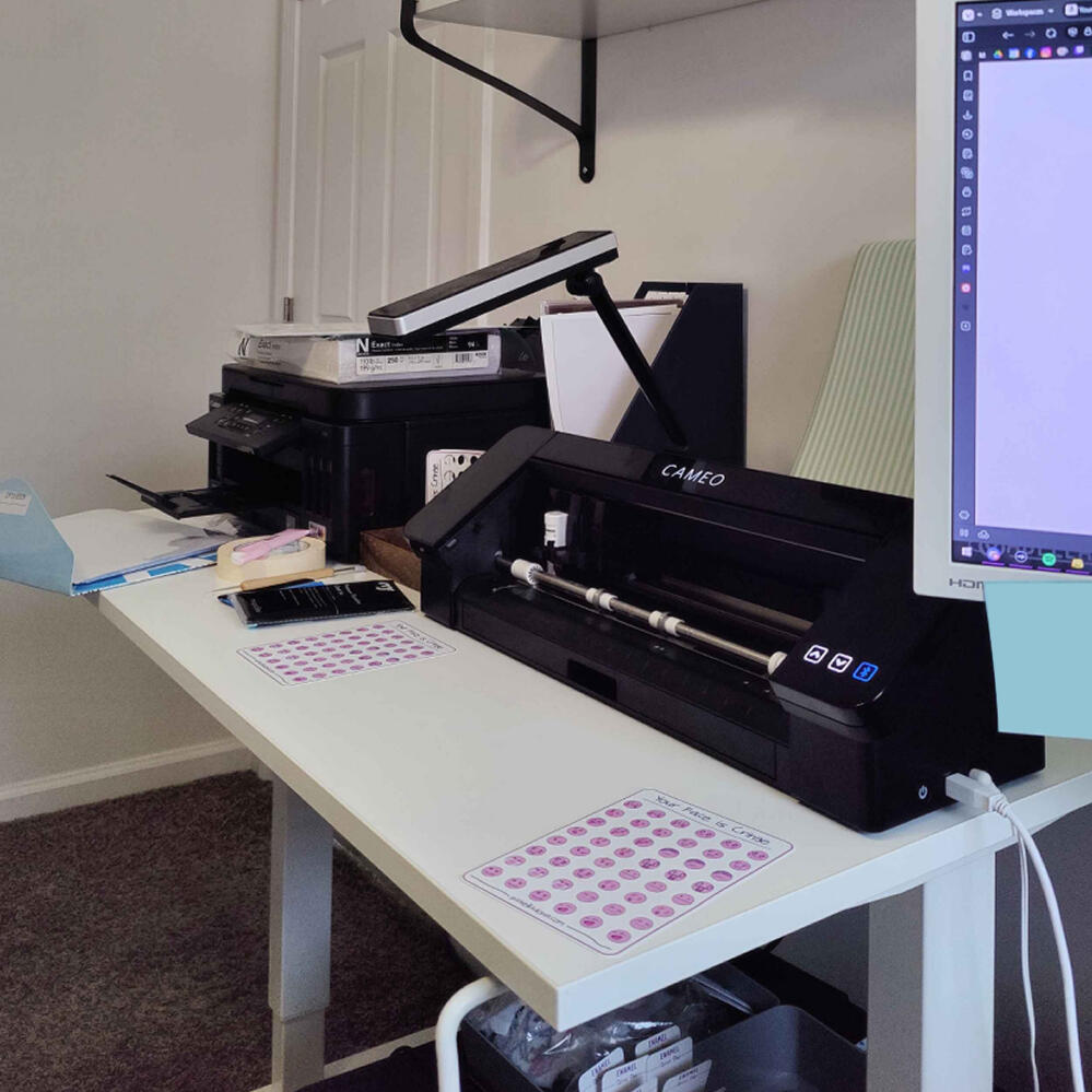 A characterization of Sabelladona the artist. She's sitting a table with a digital drawing tablet in front of her, her hand poised over the drawing surface. She's wearing a pastel pink hoodie, with a pastel blue shirt under it. She's looking at the camera